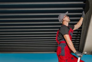 A construction worker wearing a grey cap, glasses, and red overalls is inspecting a aluminium pergola ceiling