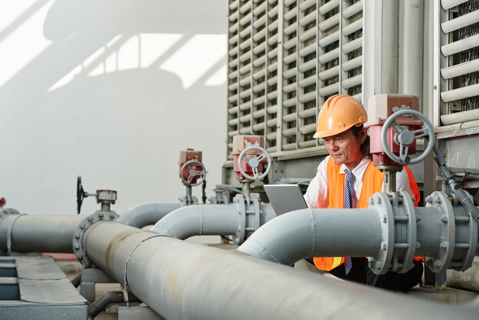 Facility manager inspecting industrial plumbing system with a laptop