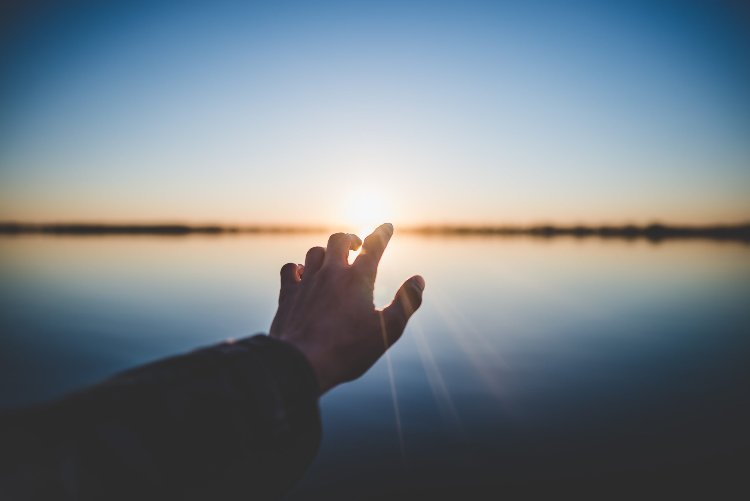 hand reaching out to the sun over a body of water
