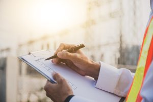 Person in safety vest writing on a checklist clipboard